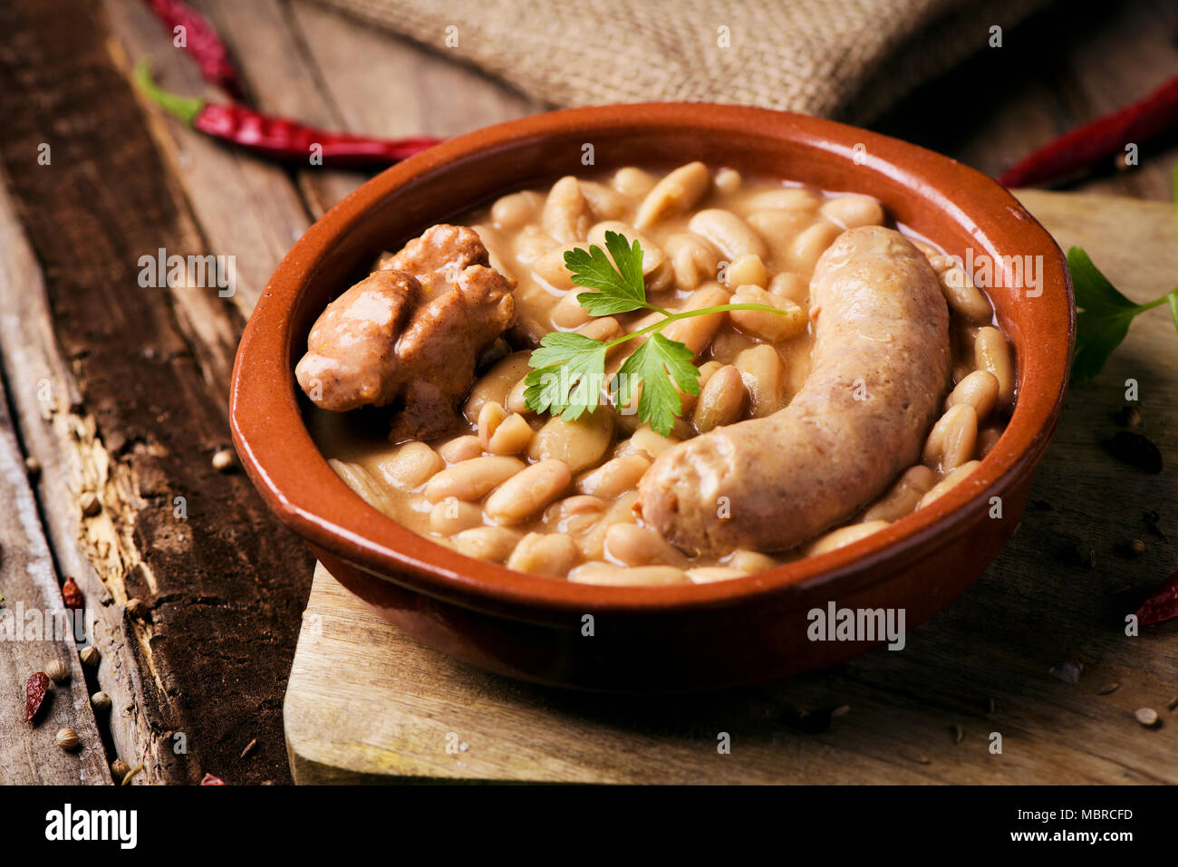closeup of an earthenware bowl with a cassoulet de Castelnaudary, a typical bean stew from Occitanie, in France, on a rustic wooden table Stock Photo