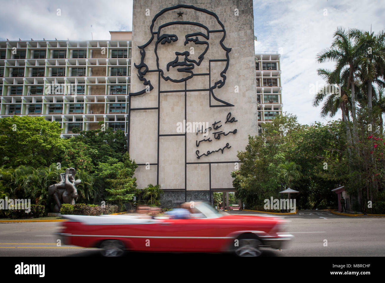 Classic American car drives past a building with a Che Guevara mural on the side in Revolution Square, Havana, Cuba. Stock Photo