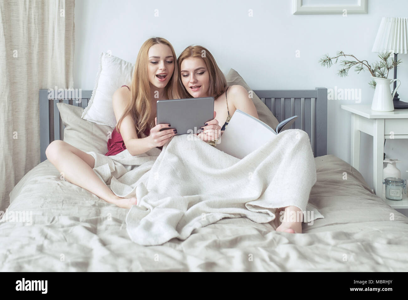 Two sexy blonde girls in pyjamas having fun in the bedroom. Young females  lying in bed using tablet Stock Photo - Alamy