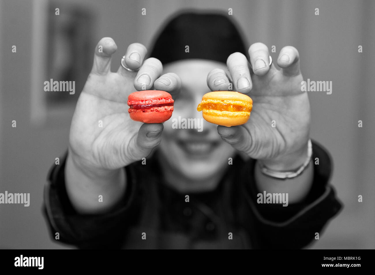 black and white capture with coloured details,  a woman holding two macarones toward the camera Stock Photo