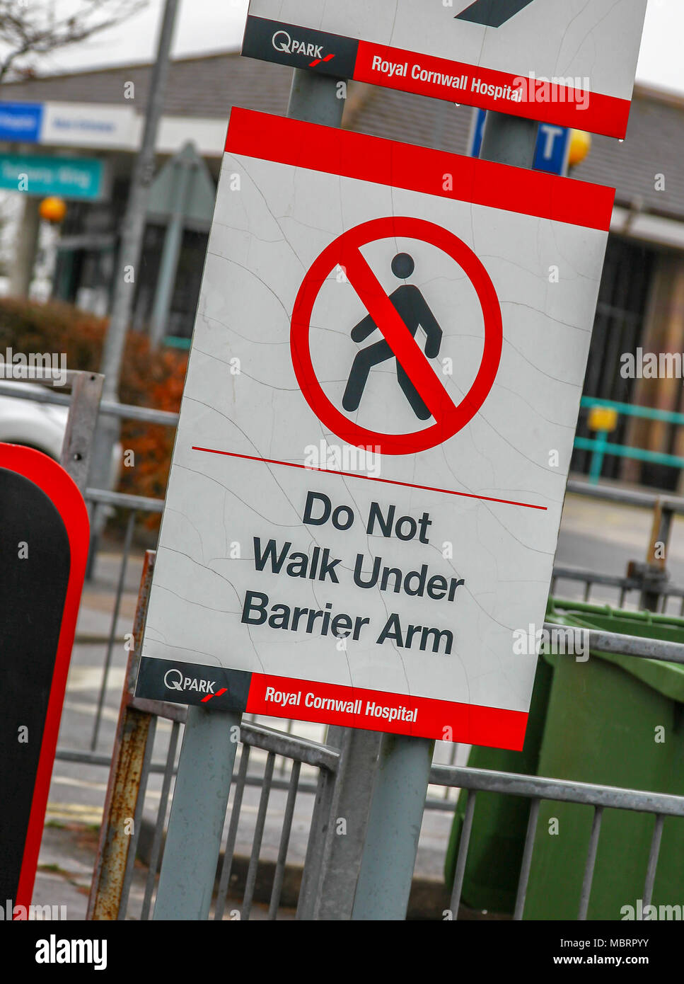 Sign warning people not to walk under a barrier arm at the entrance to a car park at Royal Cornwall Hospital, Truro, Cornwall, South West England, UK Stock Photo