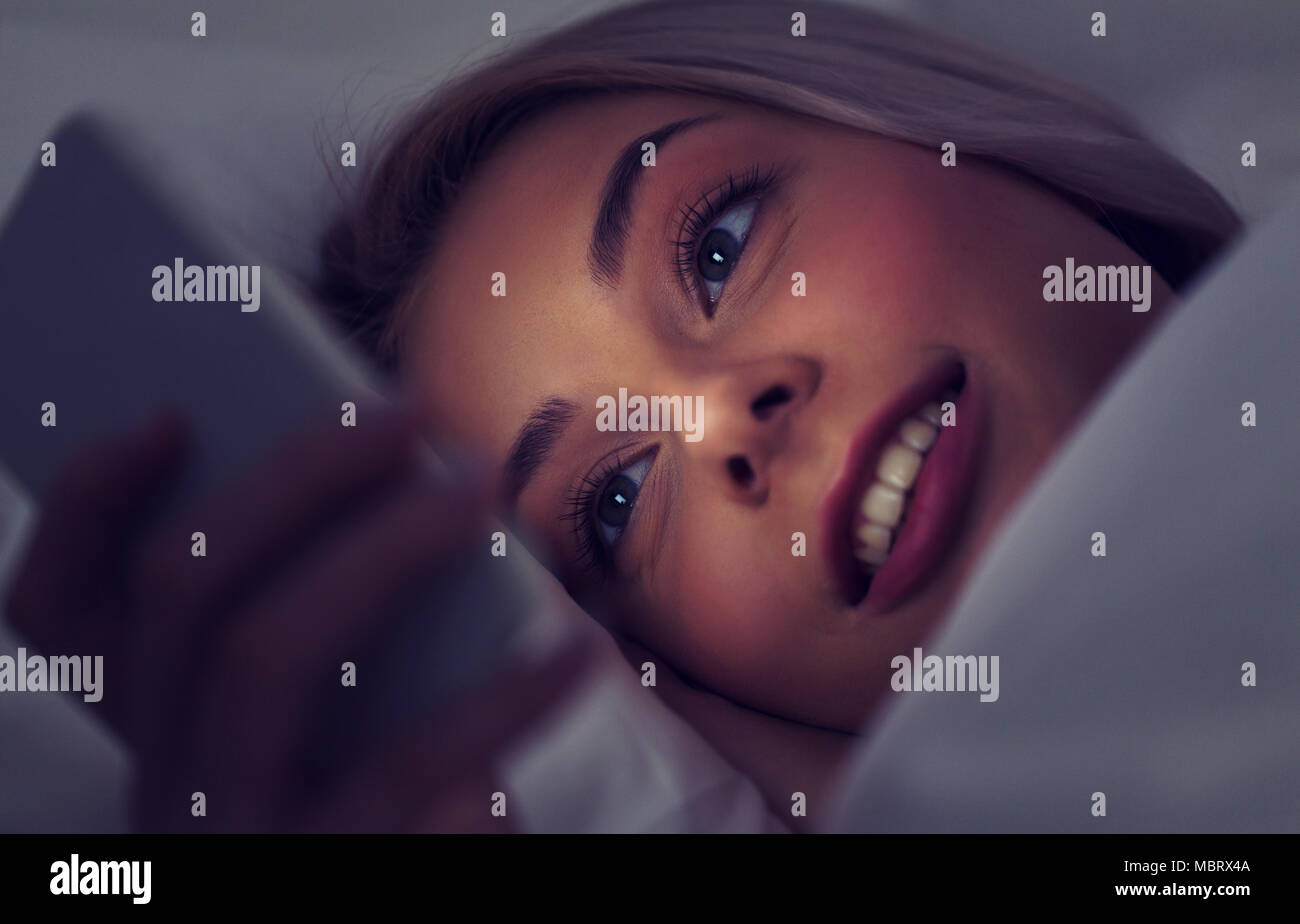 young woman with smartphone in bed at night Stock Photo