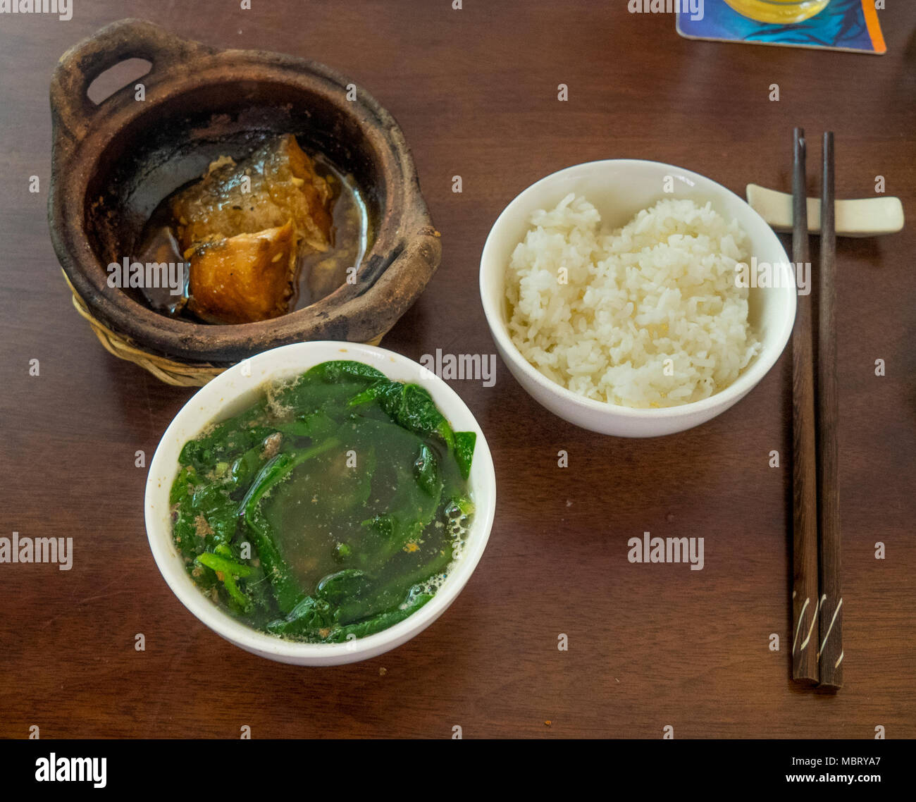 Ca kho to, a stewed claypot of catfish or basa fish and a bowl of green vegetavles, morning glory, rau muong, or water spinach, Ho Chi Minh CIty. Stock Photo