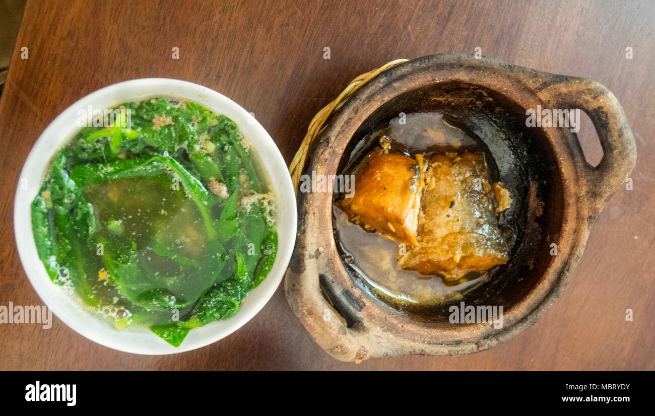 Ca kho to, a stewed claypot of catfish or basa fish and a bowl of green vegetavles, morning glory, rau muong, or water spinach, Ho Chi Minh CIty. Stock Photo