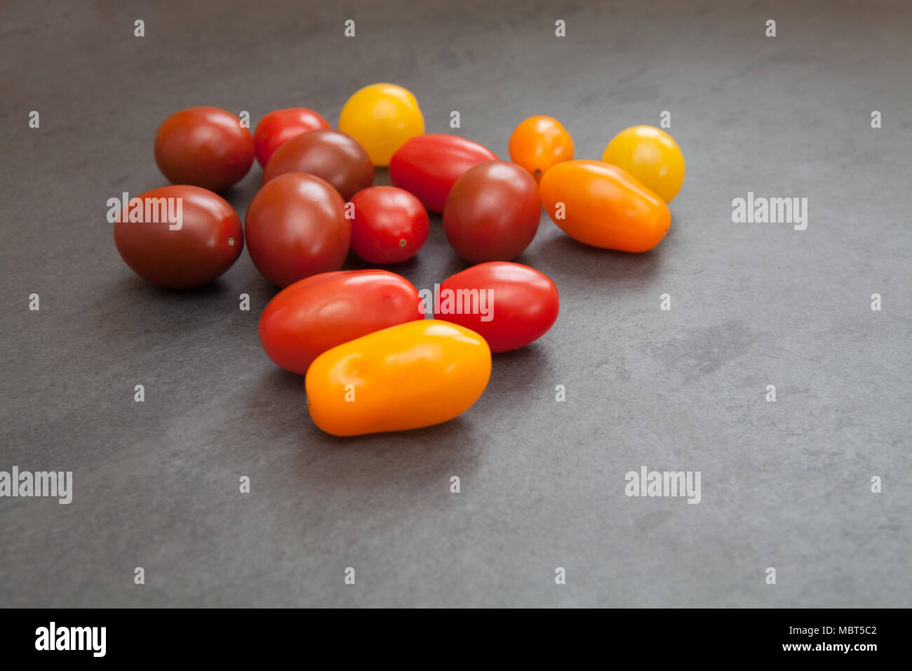 Raw ingredients: cherry and baby plum tomatoes in a variety of colours shown on a slate board Stock Photo