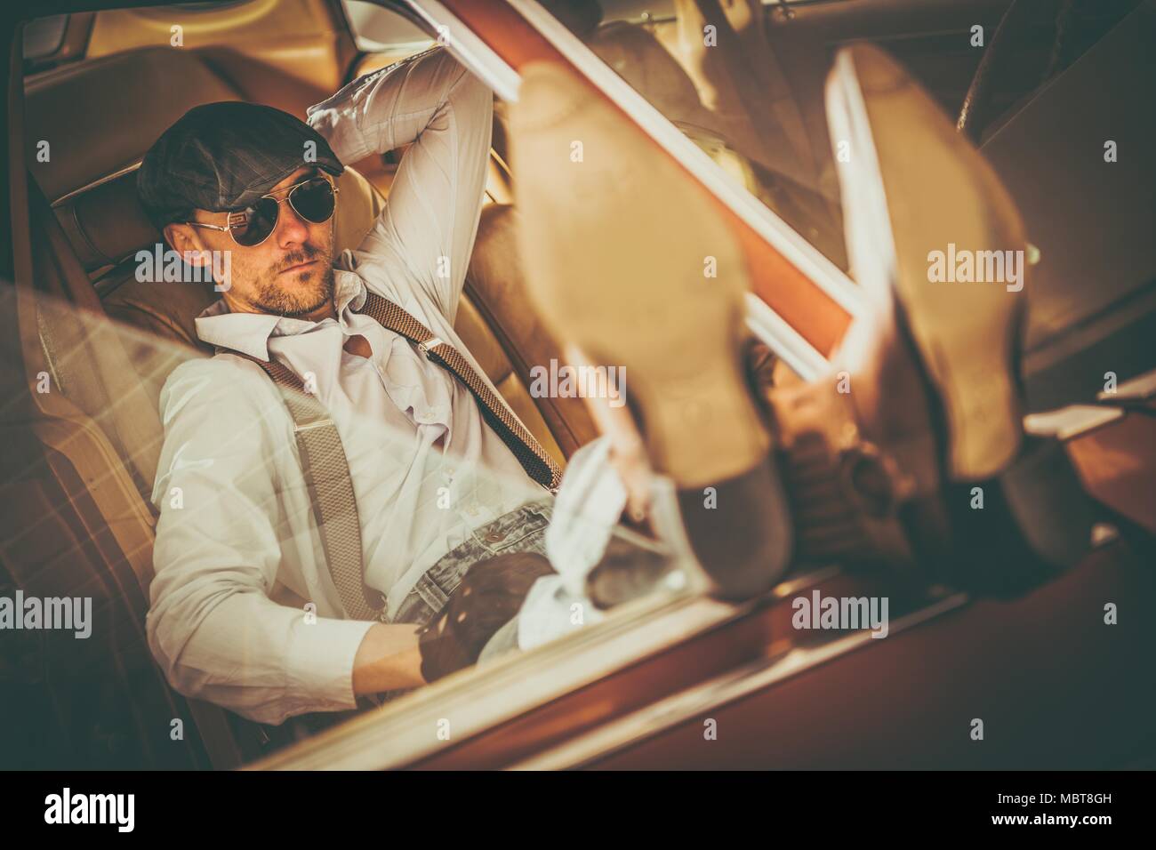 Caucasian Men in His 30s Western Wearing and Sunglasses Enjoying the Moment and in His American Classic Car Keeping His Legs on the Vehicle Door. Stock Photo