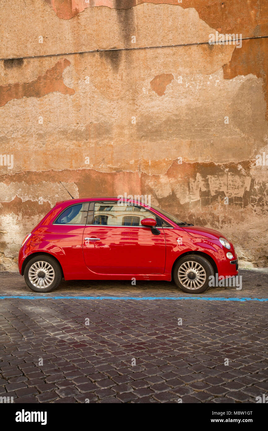 Red Fiat 500 car parked on a cobbled street in Rome, Italy, the blue line means a it's a pay to park bay with parking meters nearby where you can buy  Stock Photo