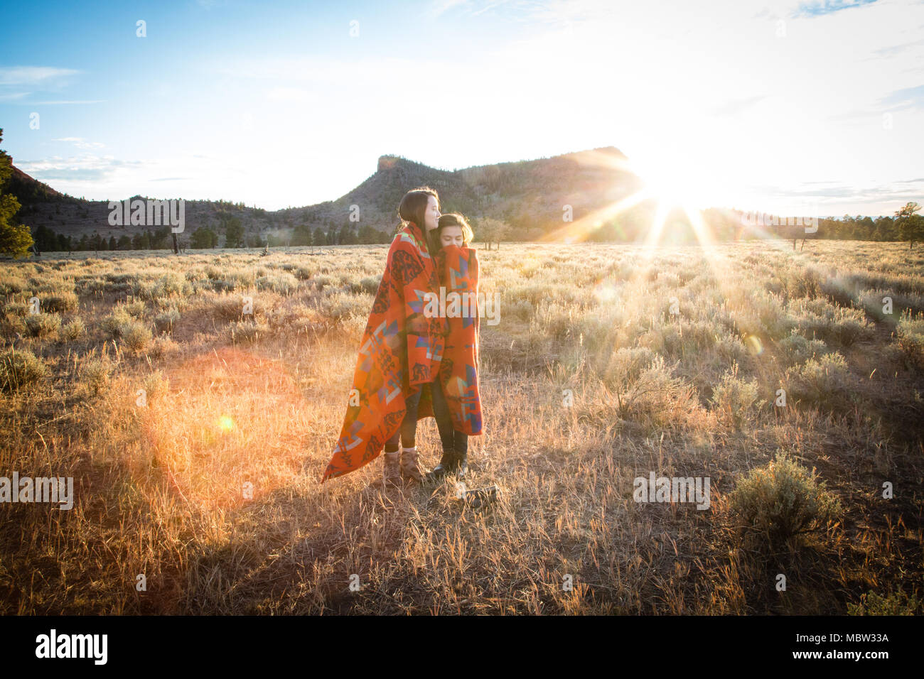Two brunette girls are wrapped in a red, native American patterned blanket at Bears Ears National Monument in southern Utah on a beautiful afternoon. Stock Photo