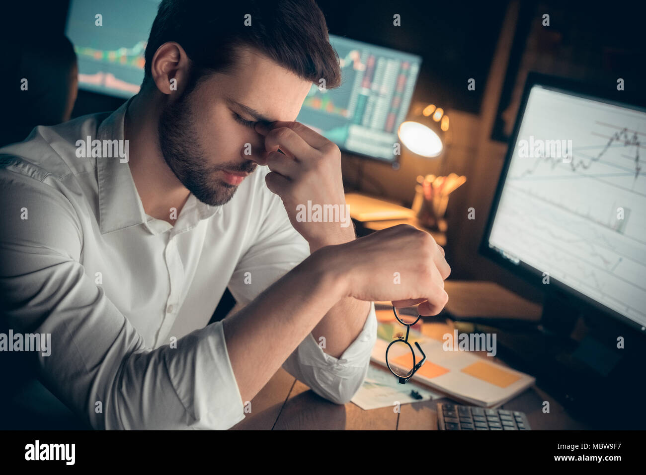 Tired businessman suffers from computer vision syndrome taking off glasses massaging eyes working late, fatigued trader feels eyestrain, has bad blurr Stock Photo