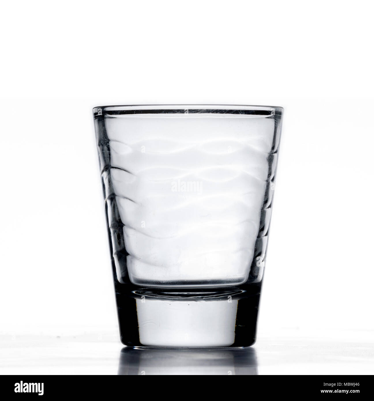 Small glass alcohol shot cup, being filled with blue water, or liquid, closeup, white background with reflection Stock Photo