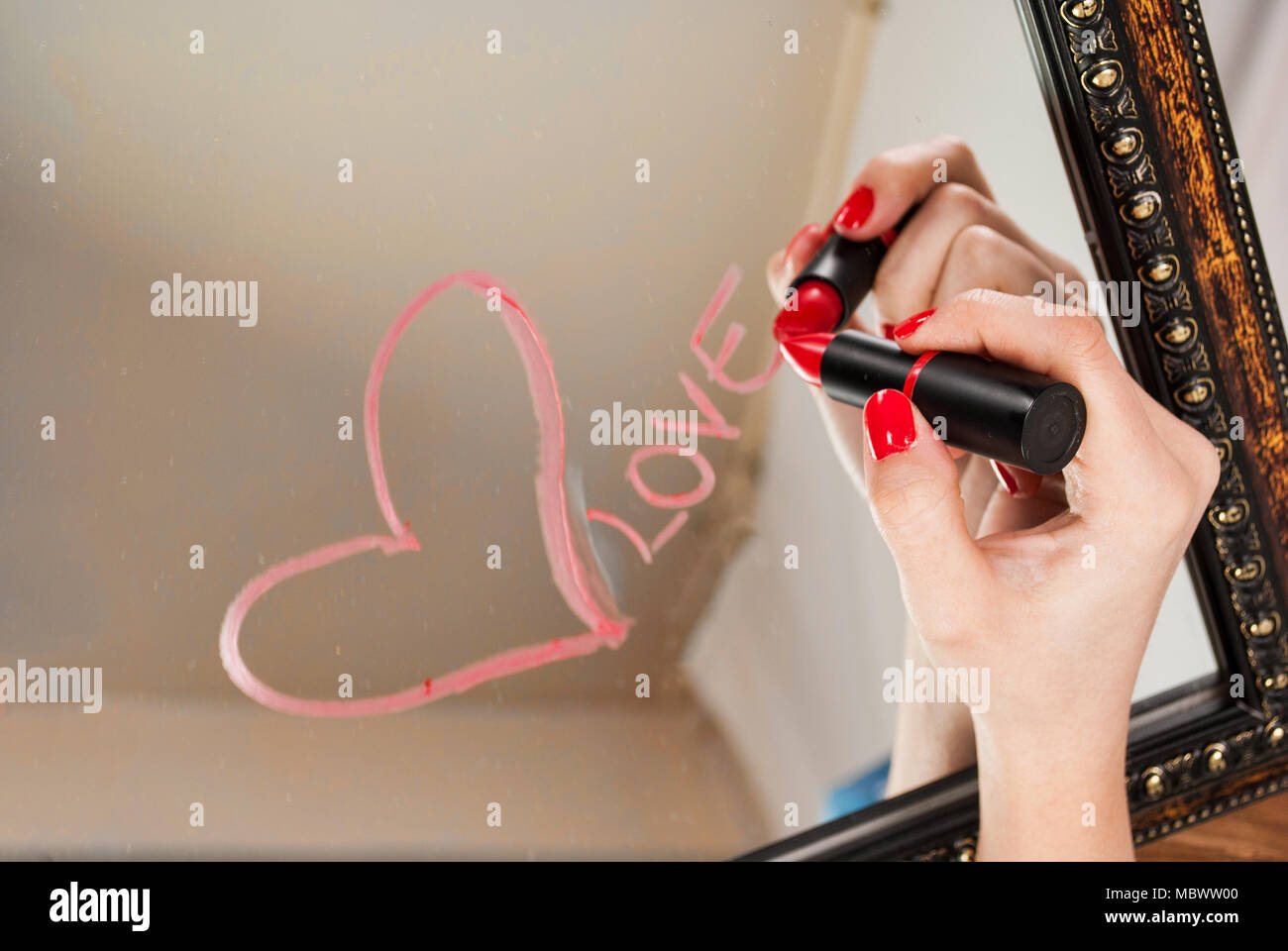 Woman hand with red lipstick drawing heart and word love on mirror for Valentines day Stock Photo