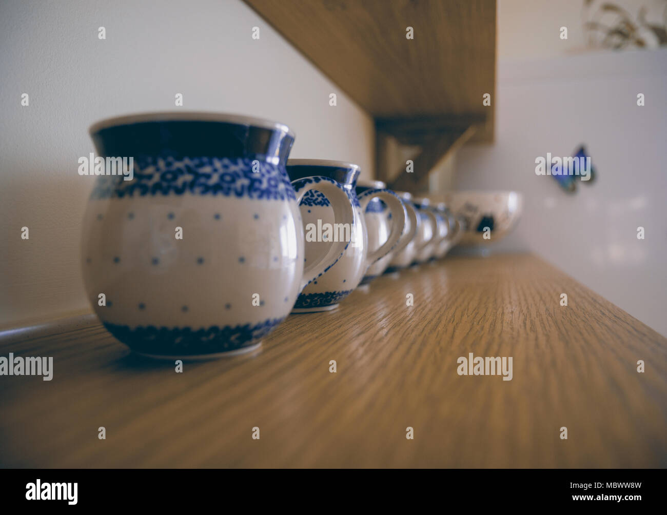 Row of thick traditionally ornamented white and blue mugs standing on the wooden shelf. Stock Photo