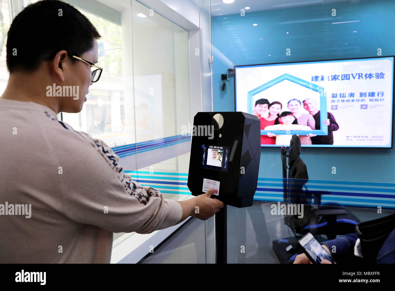 Shanghai, China. 12th Apr, 2018. A customer enters a virtual reality experience zone of a self-service area at Jiujiang Road branch of China Construction Bank (CCB) in Shanghai, east China, April 12, 2018. Customers are able to transact 90 percent of cash and non-cash business in the self-service area of the branch. Credit: Fang Zhe/Xinhua/Alamy Live News Stock Photo