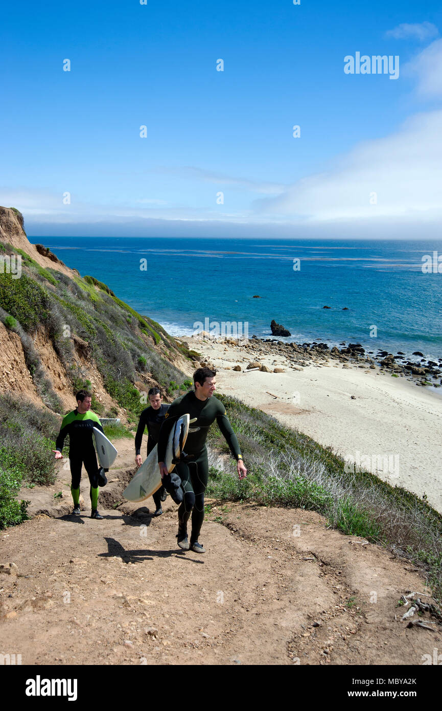 Surfers climbing up the trail from beach on the coast of Southern California near Malibu after a morning of surfing. Stock Photo