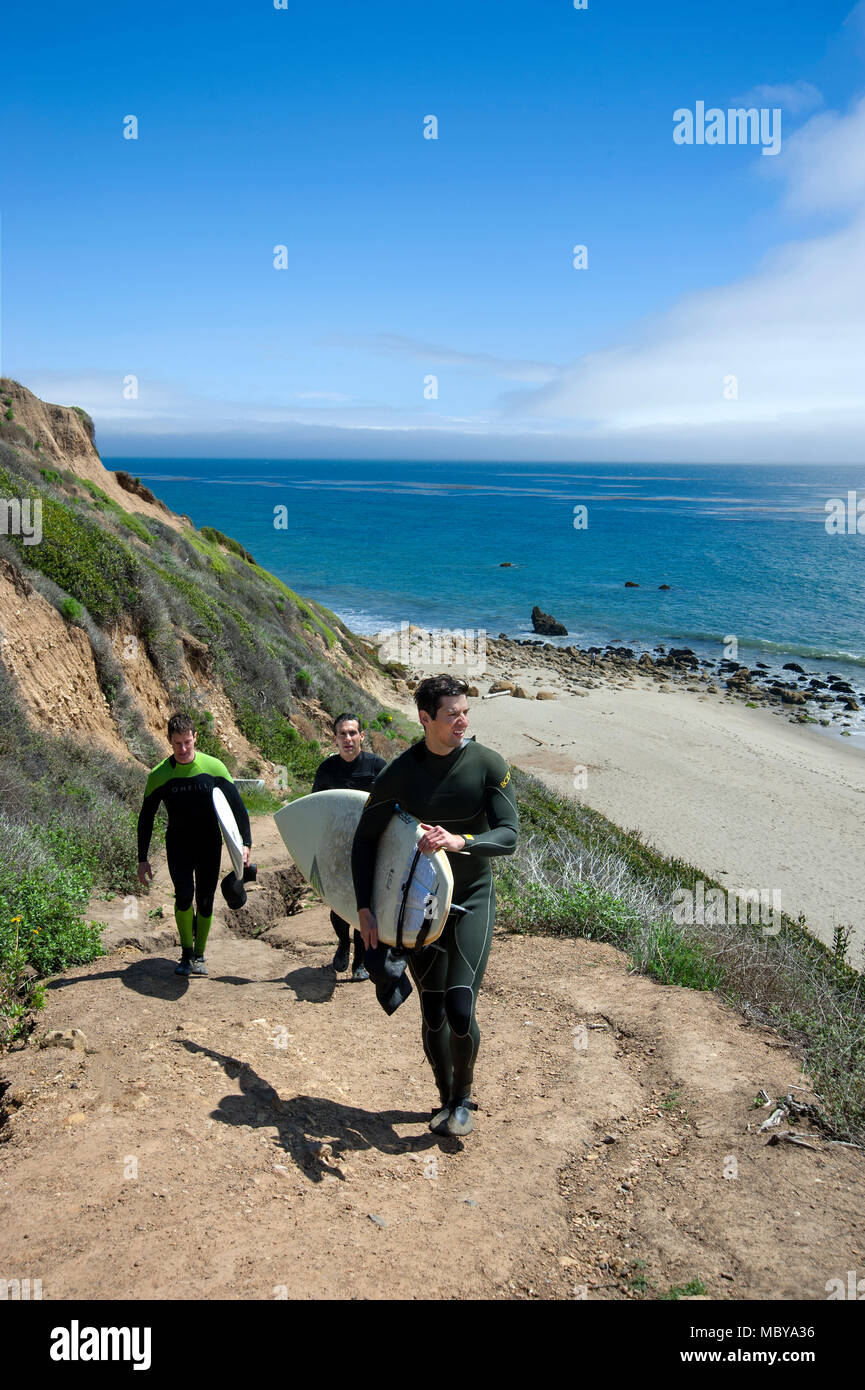 Surfers climbing up trail on cliffs above beach near Malibu, CA Stock Photo
