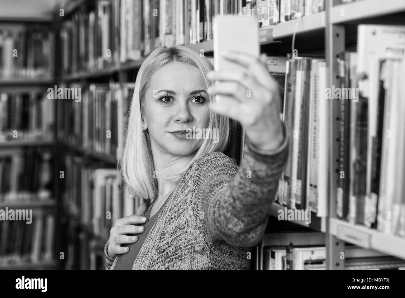 Portrait of a Happy Blonde Woman in Library at the University and Taking Selfies With Mobile Phone Stock Photo