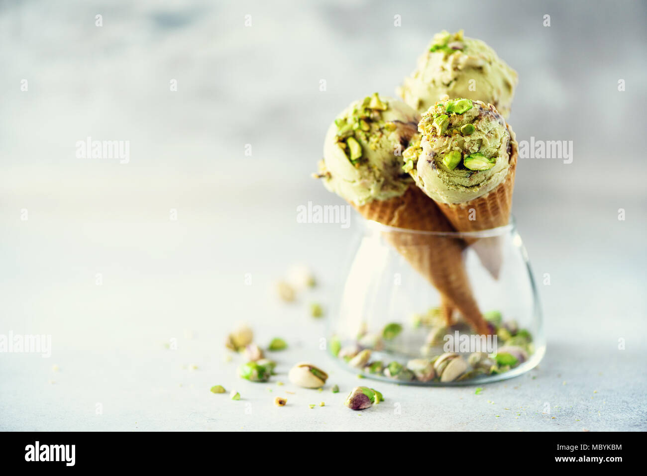 Green ice cream in waffle cone with chocolate and pistachio nuts on grey stone background. Summer food concept, copy space. Healthy gluten free ice-cream. Stock Photo