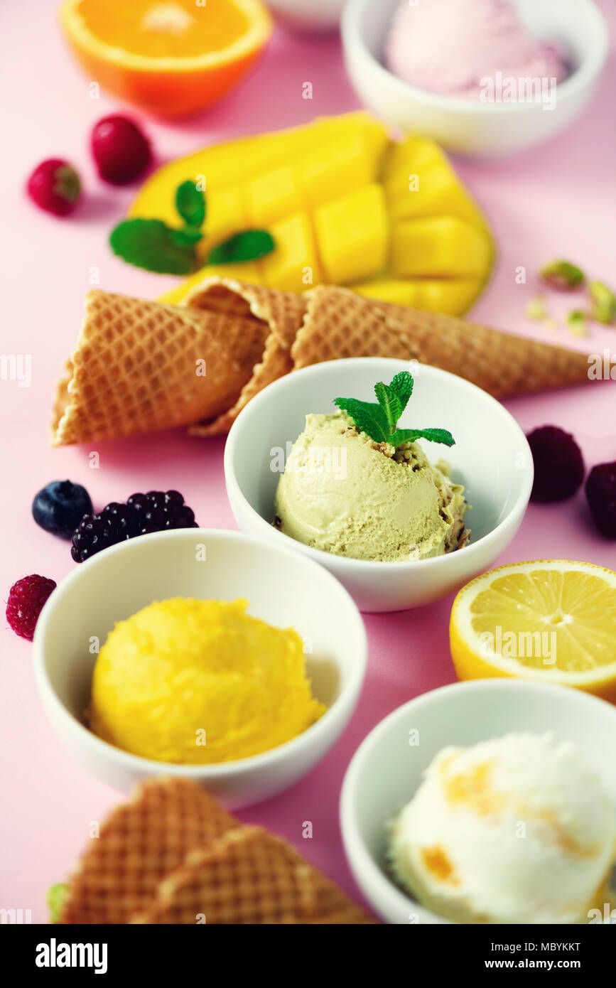 Ice cream balls in bowls, waffle cones, berries, orange, mango, lemon