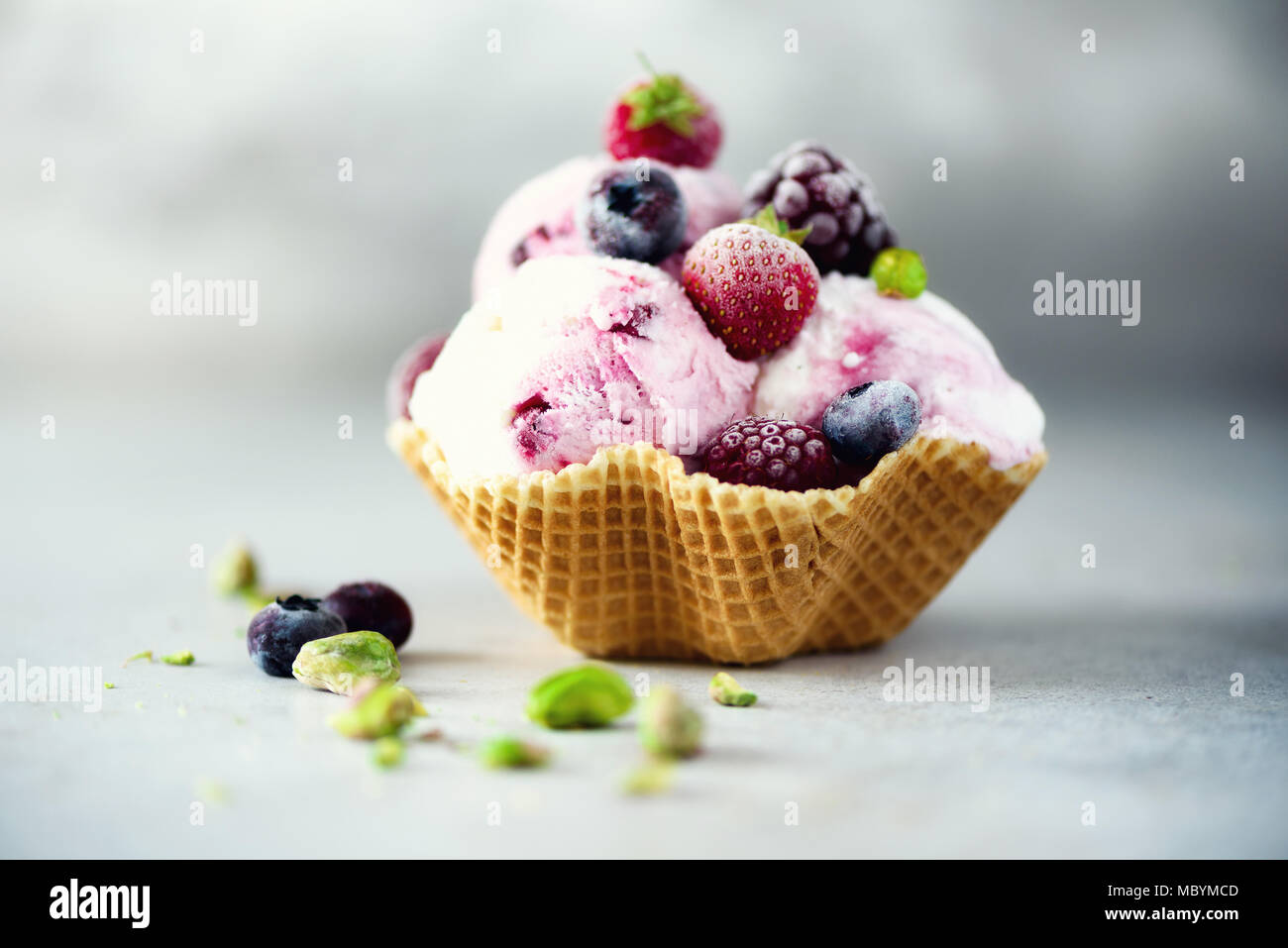 Pink ice cream with berries, strawberries, blueberries, raspberries, pistachios in waffle basket. Summer food concept, copy space. Healthy gluten free fruit ice-cream. Banner Stock Photo
