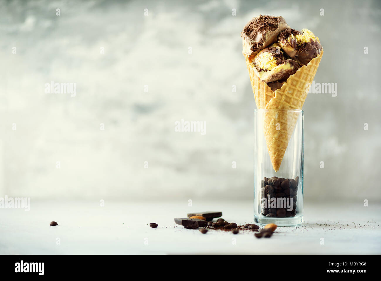 Chocolate and coffee ice cream in waffle cone with coffee beans on grey stone background. Summer