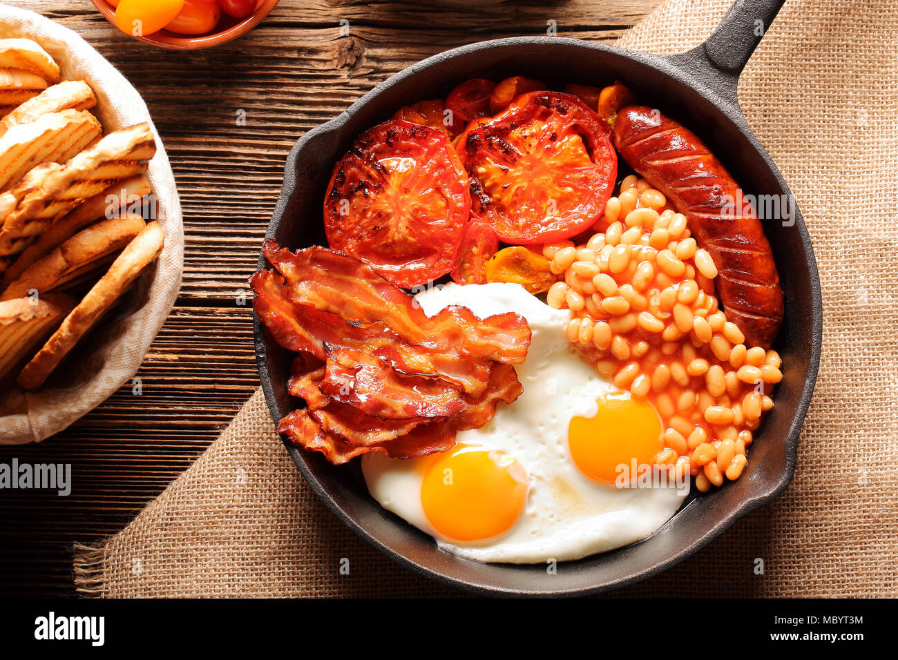 English Breakfast with sausages, grilled tomatoes, egg, bacon, beans and bread on frying pan