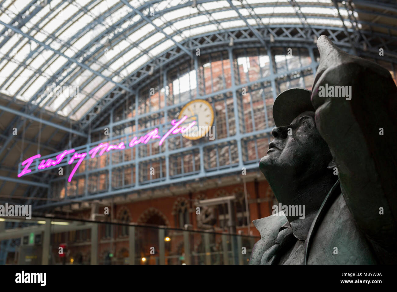 The statue of poet John Betjeman by Martin Jennings looks up to the new artwork entitled 'I Want My Time With You' by British (Britpop) artist Tracy Emin which hangs over the main concourse at St. Pancras Station, on 10th April 2018, in London, England. In the sixth year of the Terrace Wires Commission - and in celebration of the 150th anniversary of St Pancras International and the 250th anniversary of the Royal Academy of Arts, at one of London's mainline station, the London hub for Eurostar - the 20 metre-long greeting to commuters reads 'I Want My Time With You' and Emin thinks that arrivi Stock Photo