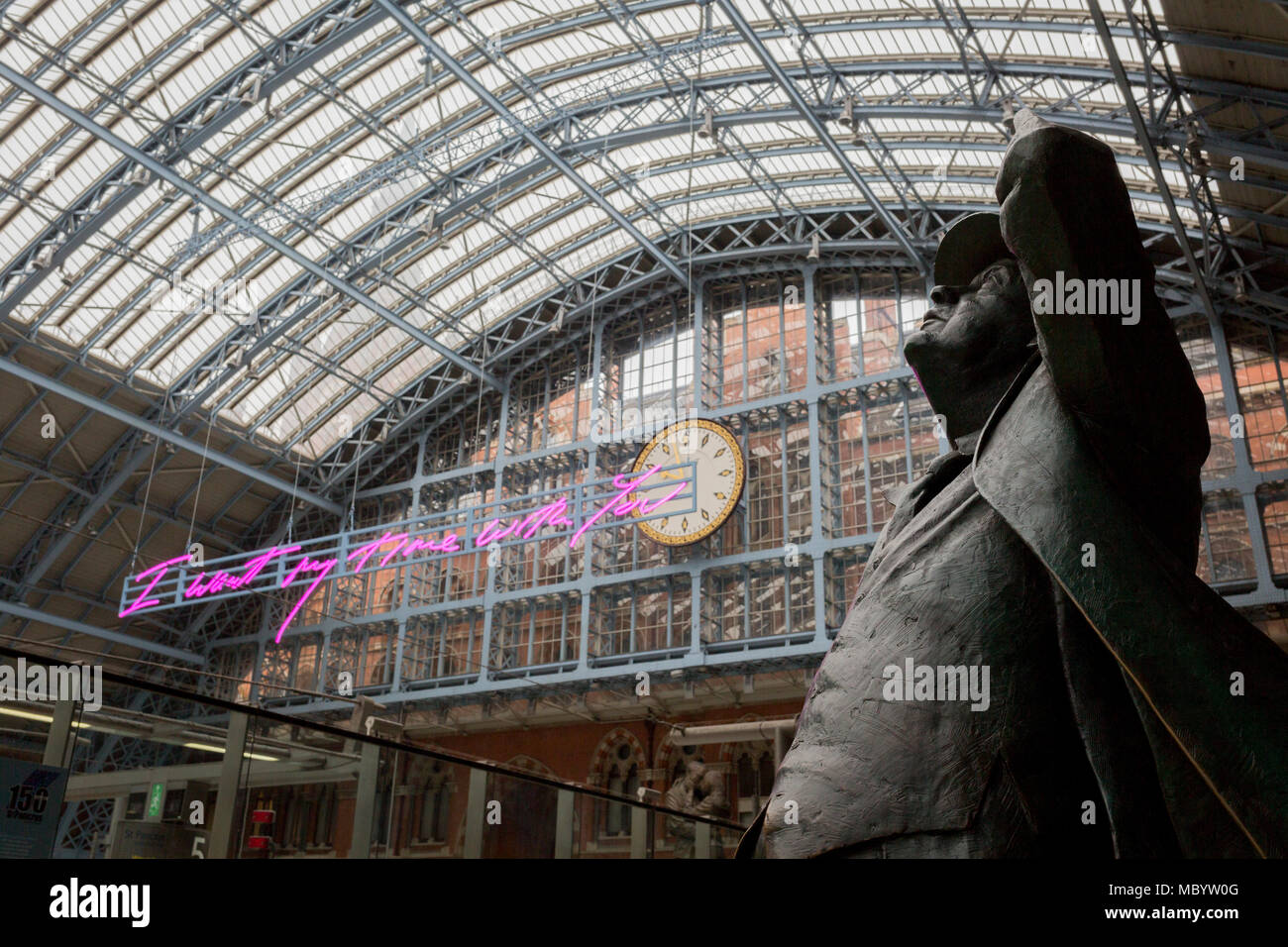The statue of poet John Betjeman by Martin Jennings looks up to the new artwork entitled 'I Want My Time With You' by British (Britpop) artist Tracy Emin which hangs over the main concourse at St. Pancras Station, on 10th April 2018, in London, England. In the sixth year of the Terrace Wires Commission - and in celebration of the 150th anniversary of St Pancras International and the 250th anniversary of the Royal Academy of Arts, at one of London's mainline station, the London hub for Eurostar - the 20 metre-long greeting to commuters reads 'I Want My Time With You' and Emin thinks that arrivi Stock Photo