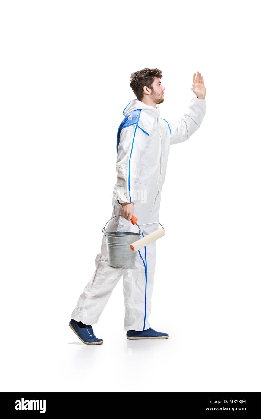 Young male decorator painting with a paint roller climbed a ladder isolated on white background. Stock Photo