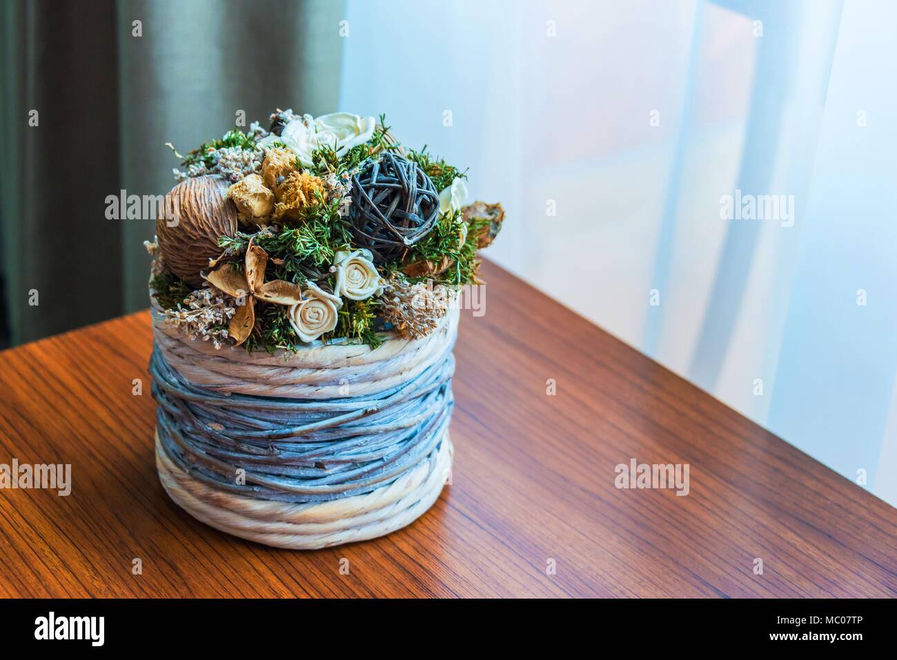 Close up of a wicker flower pot with dried flowers arrangement over a wooden table by the window. Stock Photo