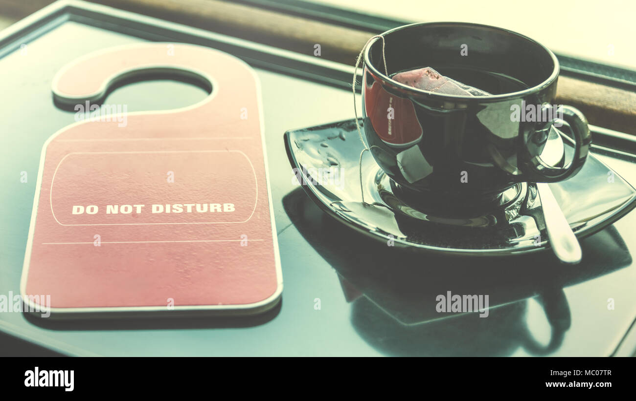 Do not disturb sign and a cup of tea over a dark tray by the window. Time for rest concept. Stock Photo