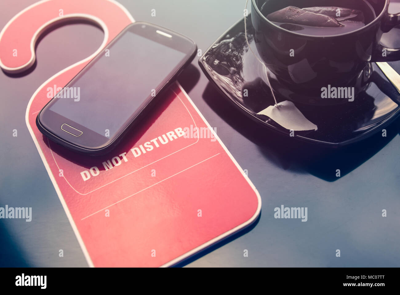 Do not disturbe sign, a cup of tea and a mobile phone over dark background. Time for rest concept. Stock Photo