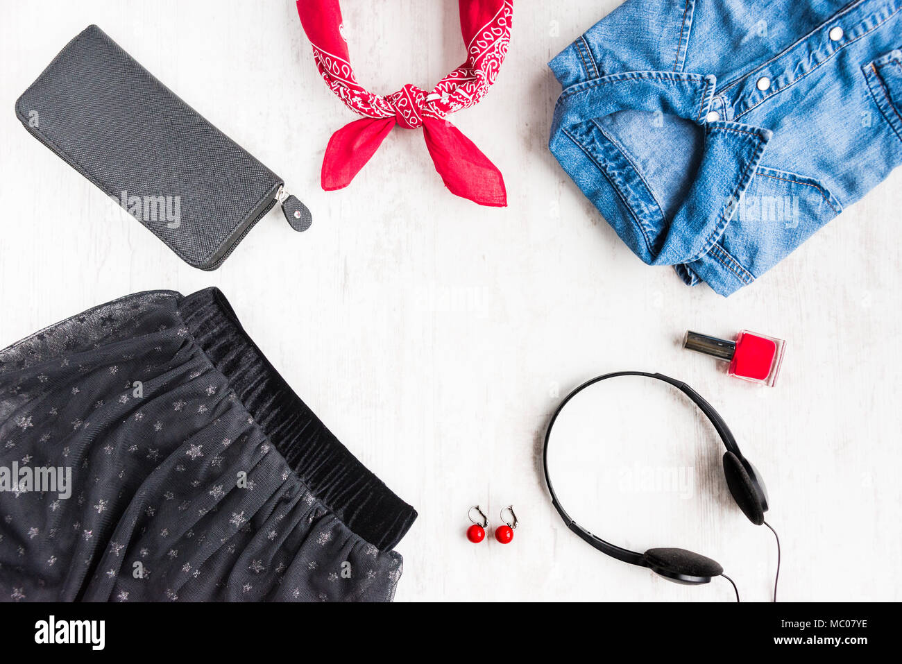 Top view of yong woman clothes and accessories. Tulle skirt, denim shirt, wallet, head phones, earrings, nail polish and kerchief. Urban style concept Stock Photo