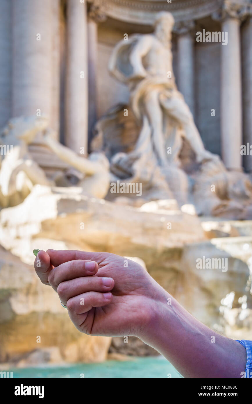Close up of a man's hand holding a coin in front of Fountain Di Trevi in Rome, Italy. Stock Photo