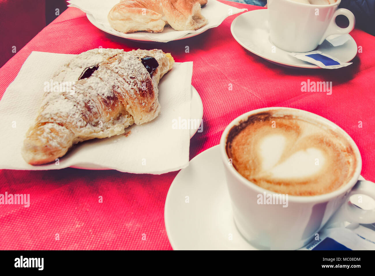 Morning breakfast in an italian restaurant - croissant and a cup of coffee with a heart shaped foam. Stock Photo