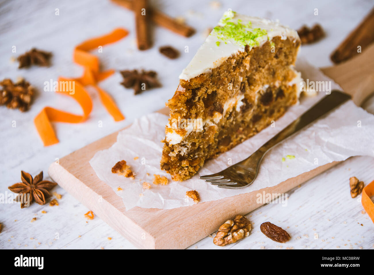 Close up of a homemade carrot cake with raisins, walnuts and cinnamon over white wooden background. Cream cheese frosting. Stock Photo