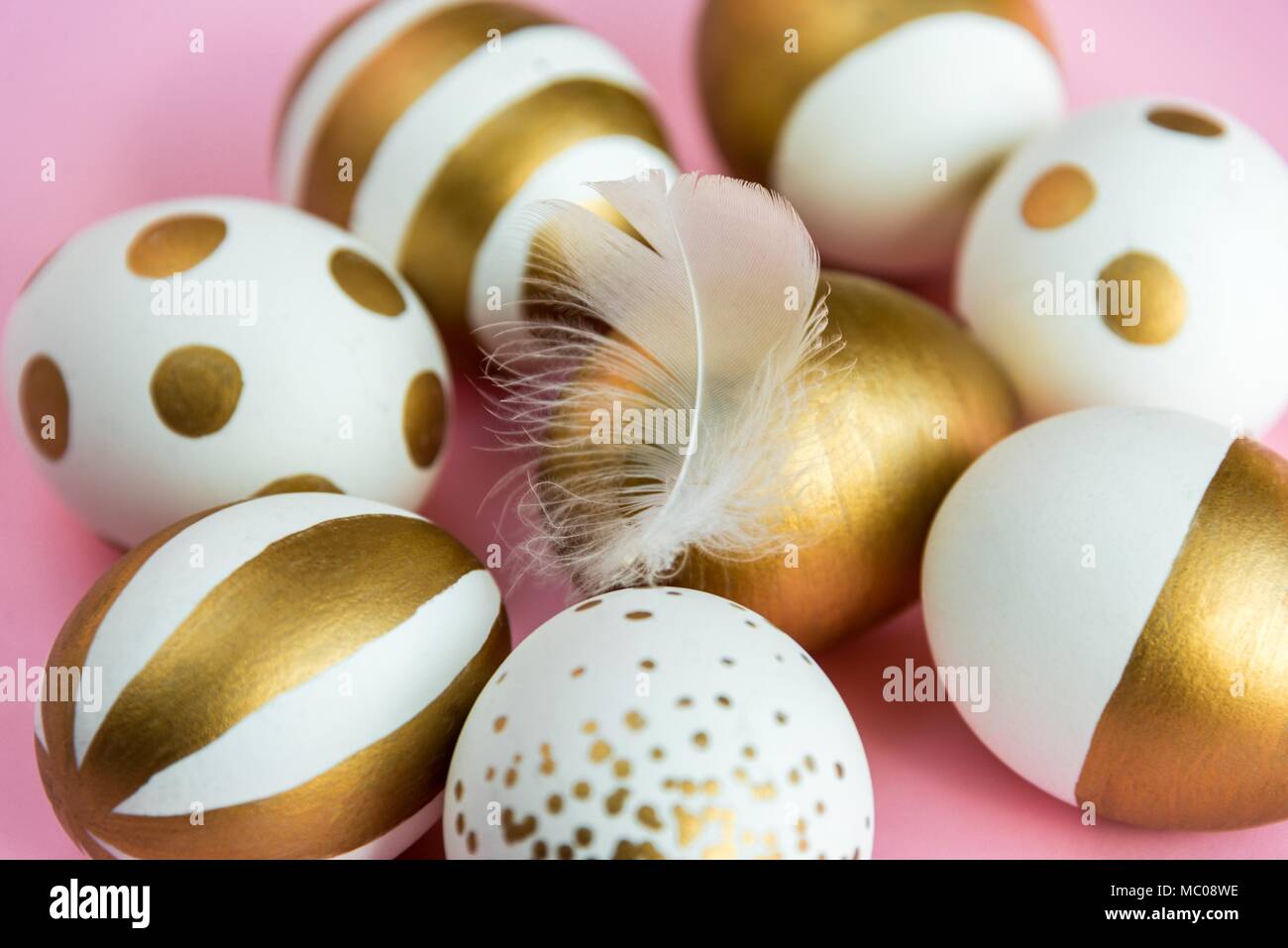 Close up of easter eggs colored with golden paint. Various striped and dotted designs. Pink background. Stock Photo