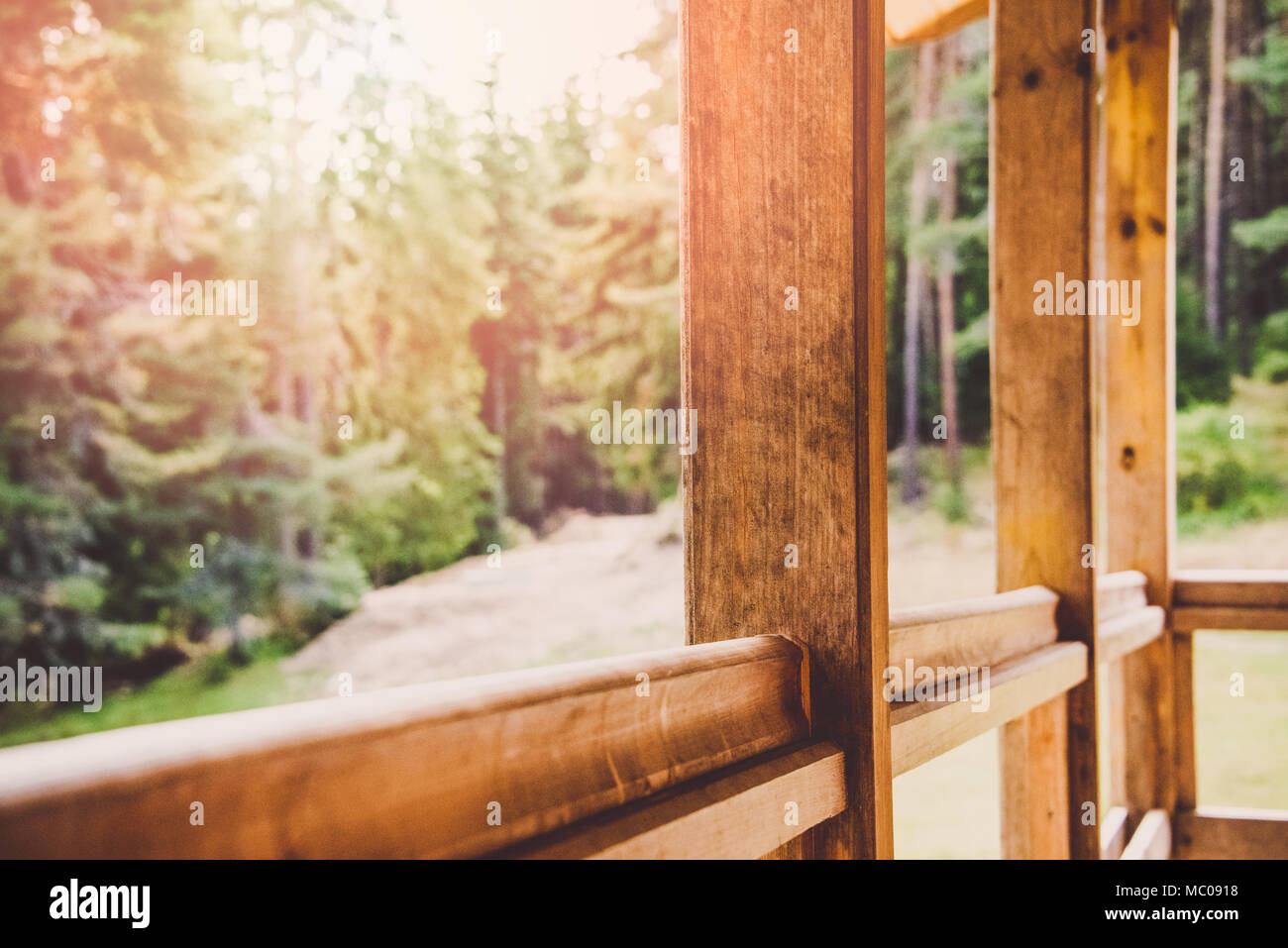 Close up of a wooden veranda parapet. Pine forest under the sun rays in the background. Stock Photo