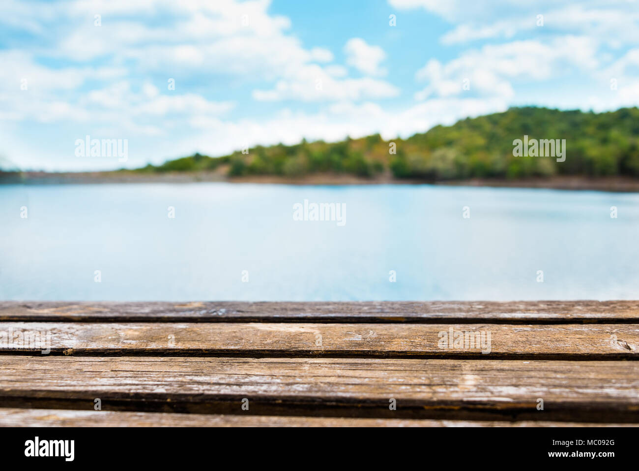 Close view of an old wooden table. Blue lake and sky in the background. Stock Photo