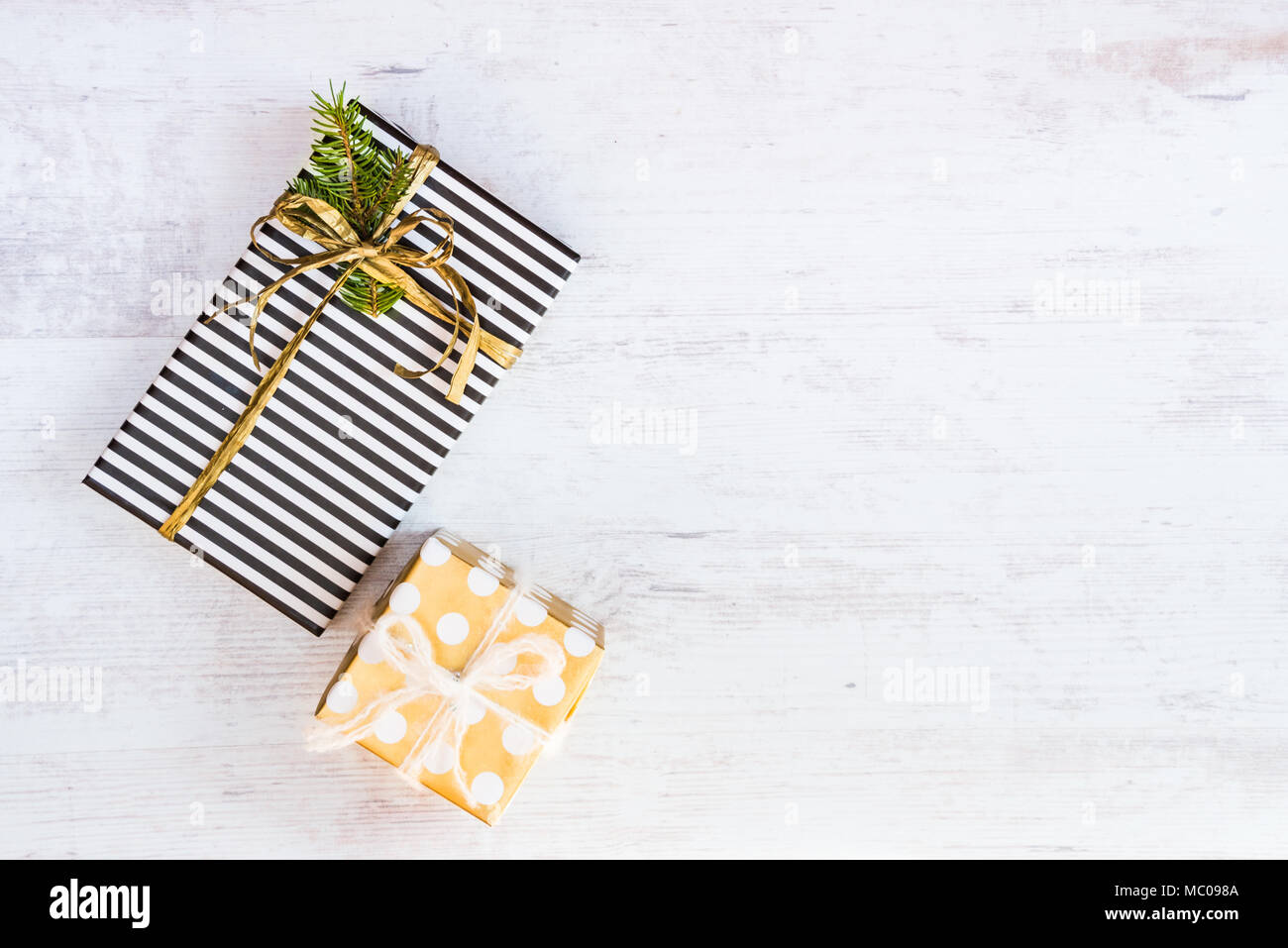 Gift boxes wrapped in black and white striped and golden dotted paper on a white wood background. Christmas presents. Empty space. Stock Photo