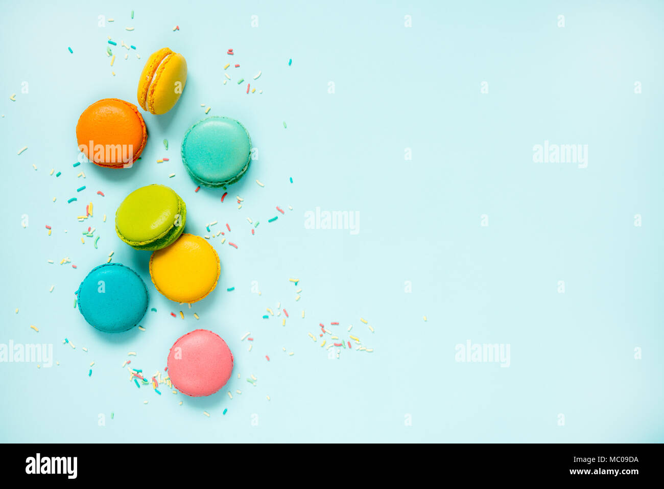 Colorful macaroons and sugar sprinkles arranged over blue background. Copy space. Stock Photo