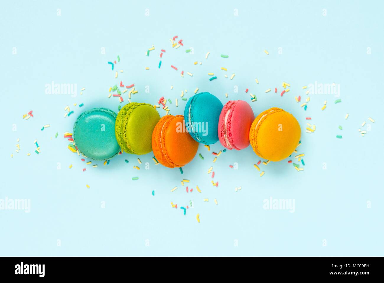 Top view of colorful macaroons and sugar sprinkles arranged over blue background. Stock Photo