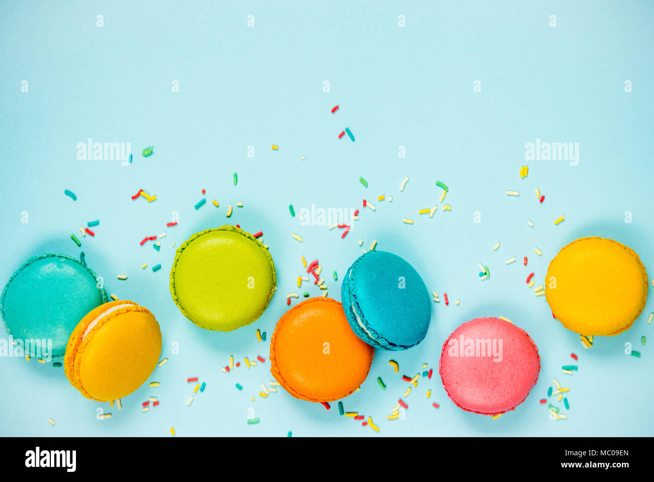 Top view of colorful macaroons and sugar sprinkles arranged over blue background. Stock Photo