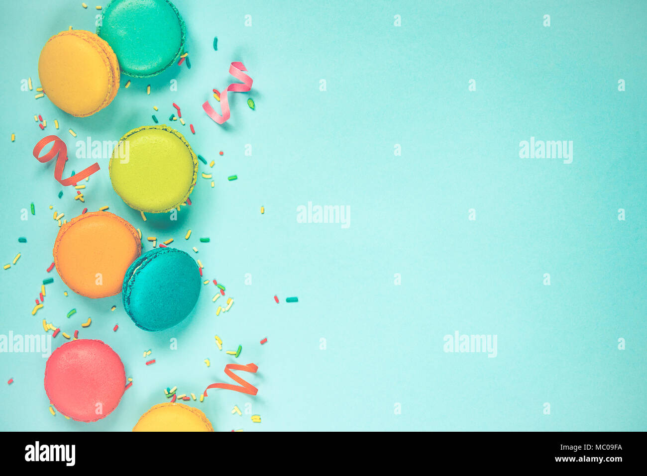 Top view of colorful macaroons, sugar sprinkles and party ribbons arranged over blue background. Copy space. Vintage effect. Stock Photo