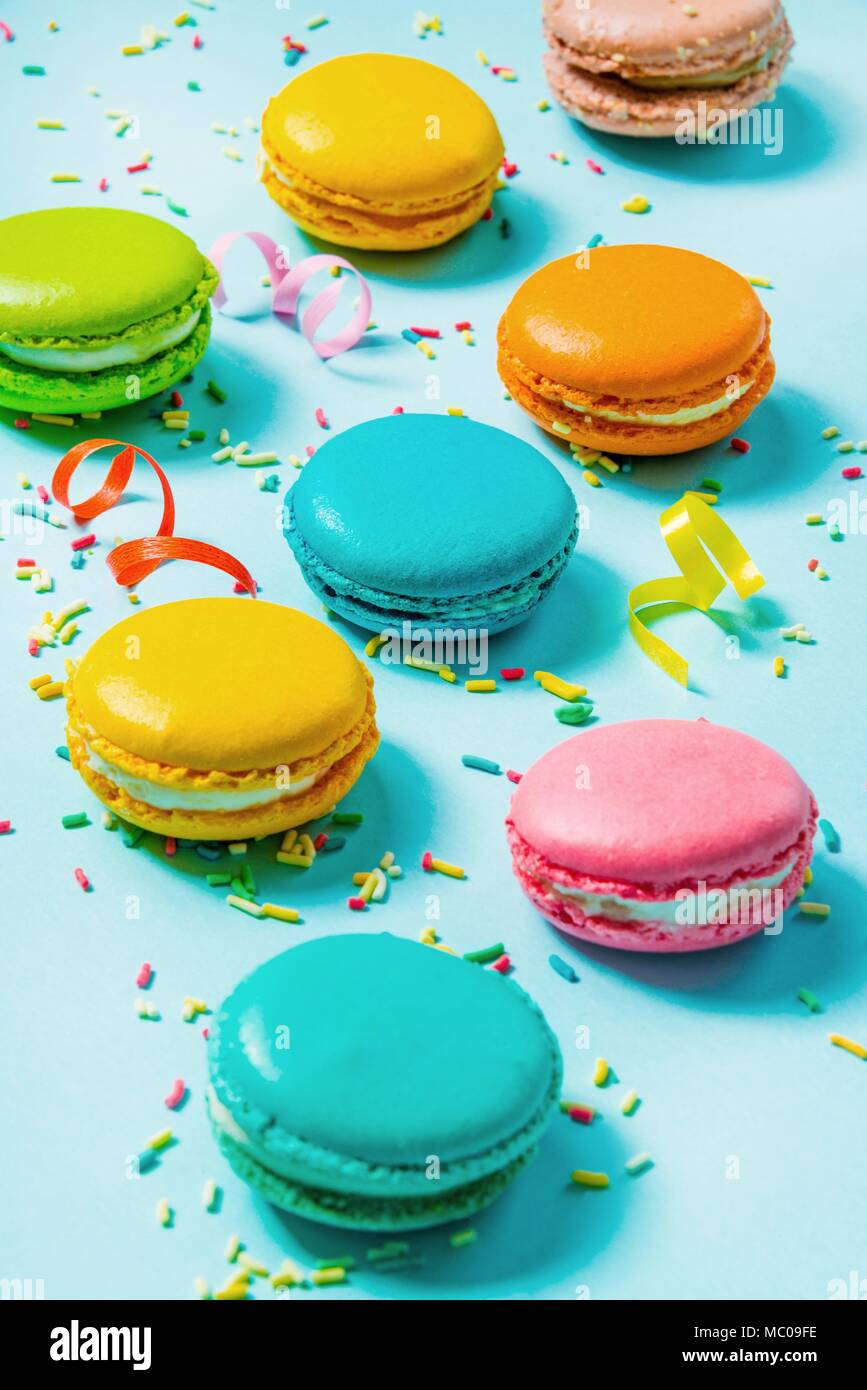 Close up of colorful macaroons, sugar sprinkles and party ribbons over blue background. Stock Photo