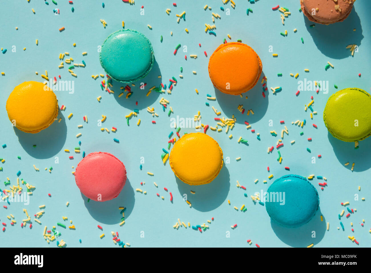 Top view of scattered colorful macaroons and sugar sprinkles over blue background. Abstract food background. Stock Photo