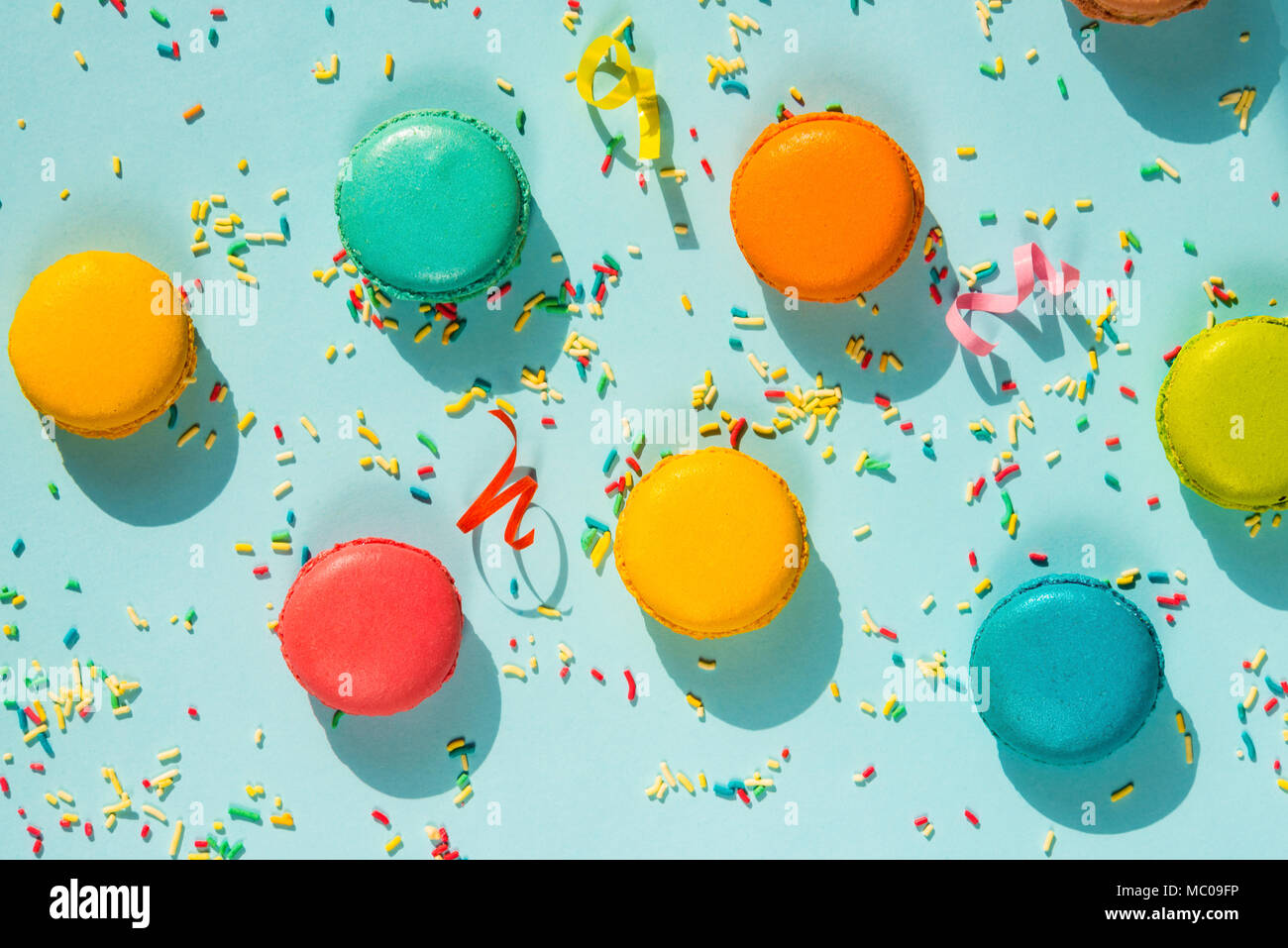 Top view of colorful macaroons, sugar sprinkles and party ribbons over blue background. Abstract party food background. Stock Photo