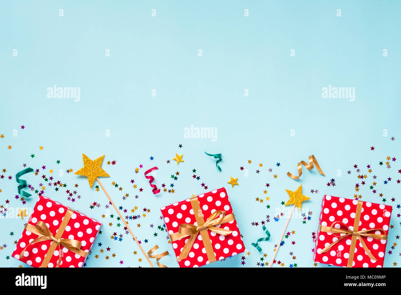 Top view of a red dotted gift boxes, golden magic wands, colorful confetti and ribbons over blue background. Celebration concept. Copy space. Stock Photo