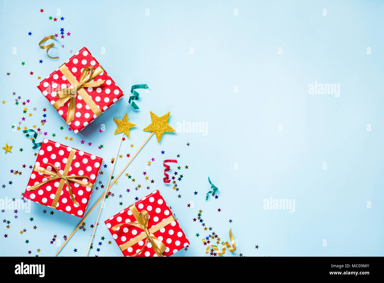 Top view of a red dotted gift boxes, golden magic wands, colorful confetti and ribbons over blue background. Celebration concept. Copy space. Stock Photo