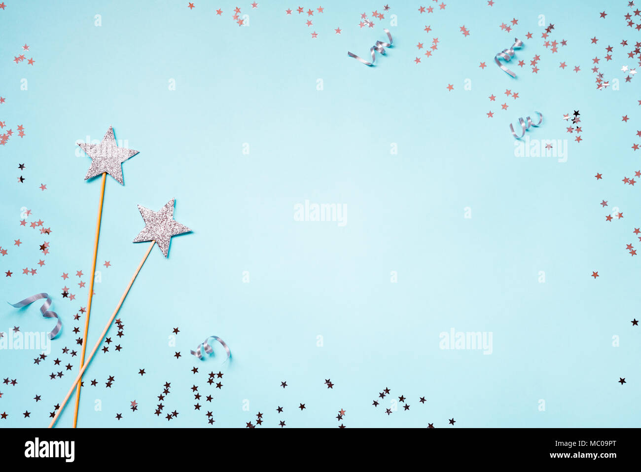 Two silver party magic wands, sequins and ribbons on a blue background. Copy space. Stock Photo