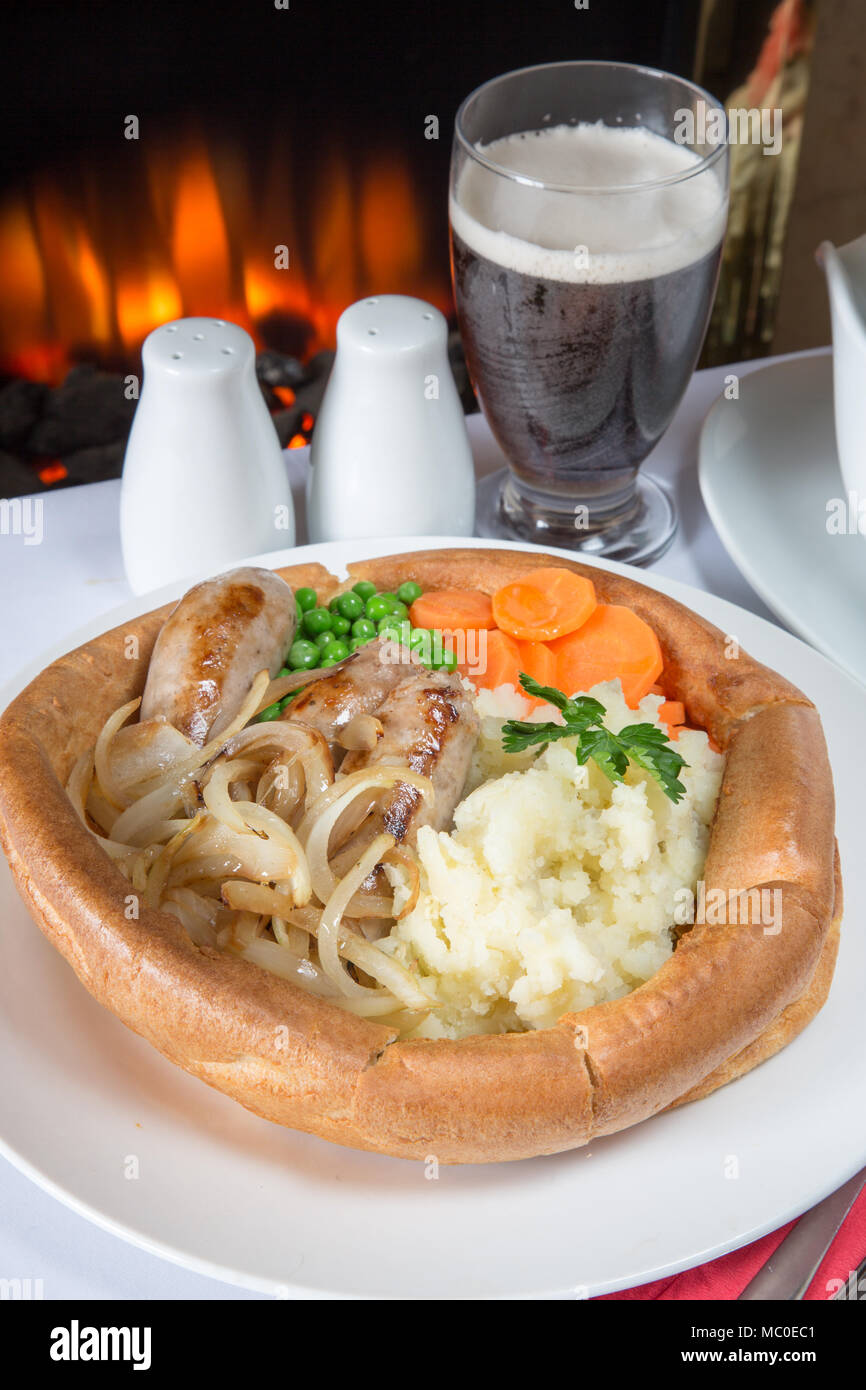 An English pub/restaurant lunch of giant Yorkshire pudding filled with Sausage and onions, creamed potato, vichy carrots, garden peas and gravy Stock Photo